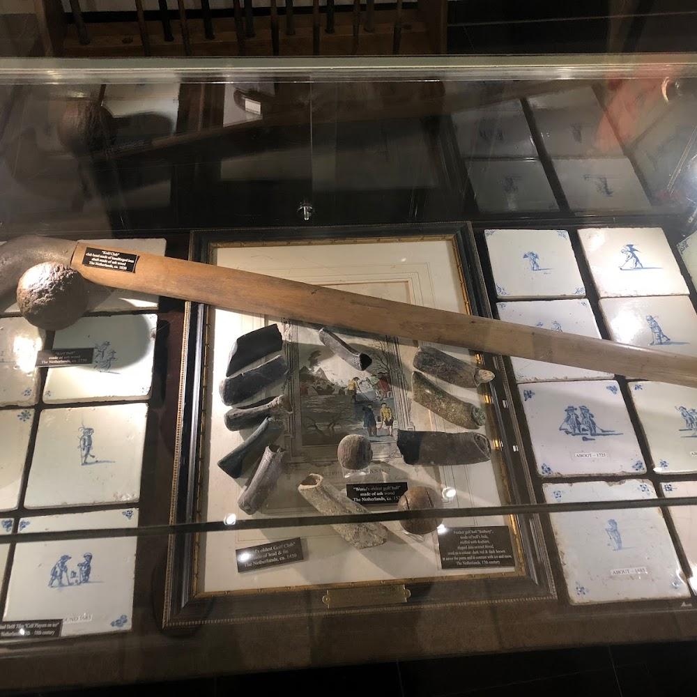 A wooden club, golf balls, and tiles in a display case. The Netherlands.